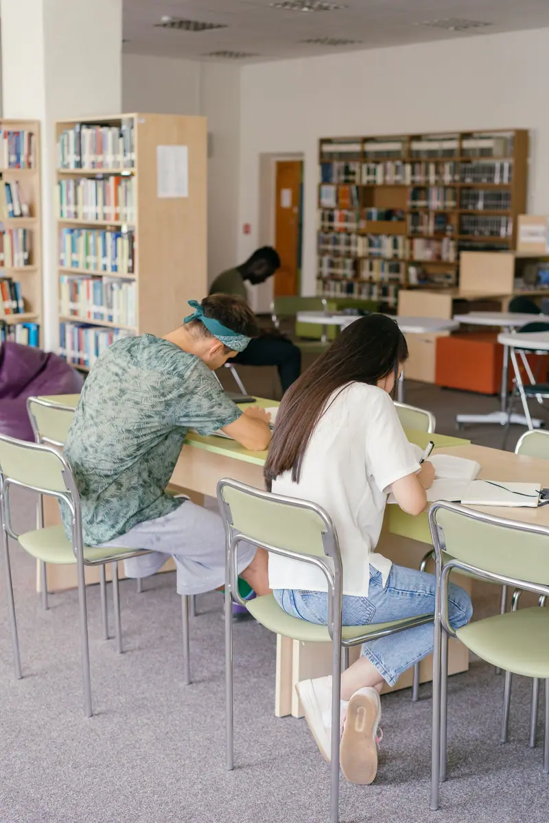 To voksne studenter som skriver notater ved et bord i et bibliotek